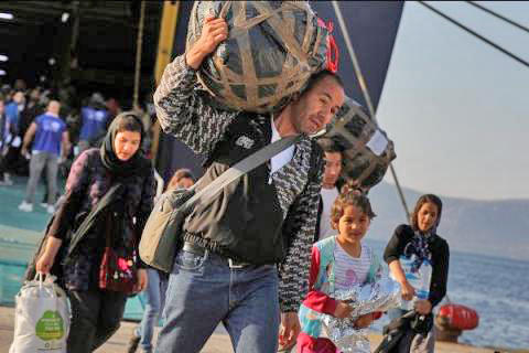 Un hombre que lleva sus pertenencias a la espalda camina frente a su familia cuando salen del barco.