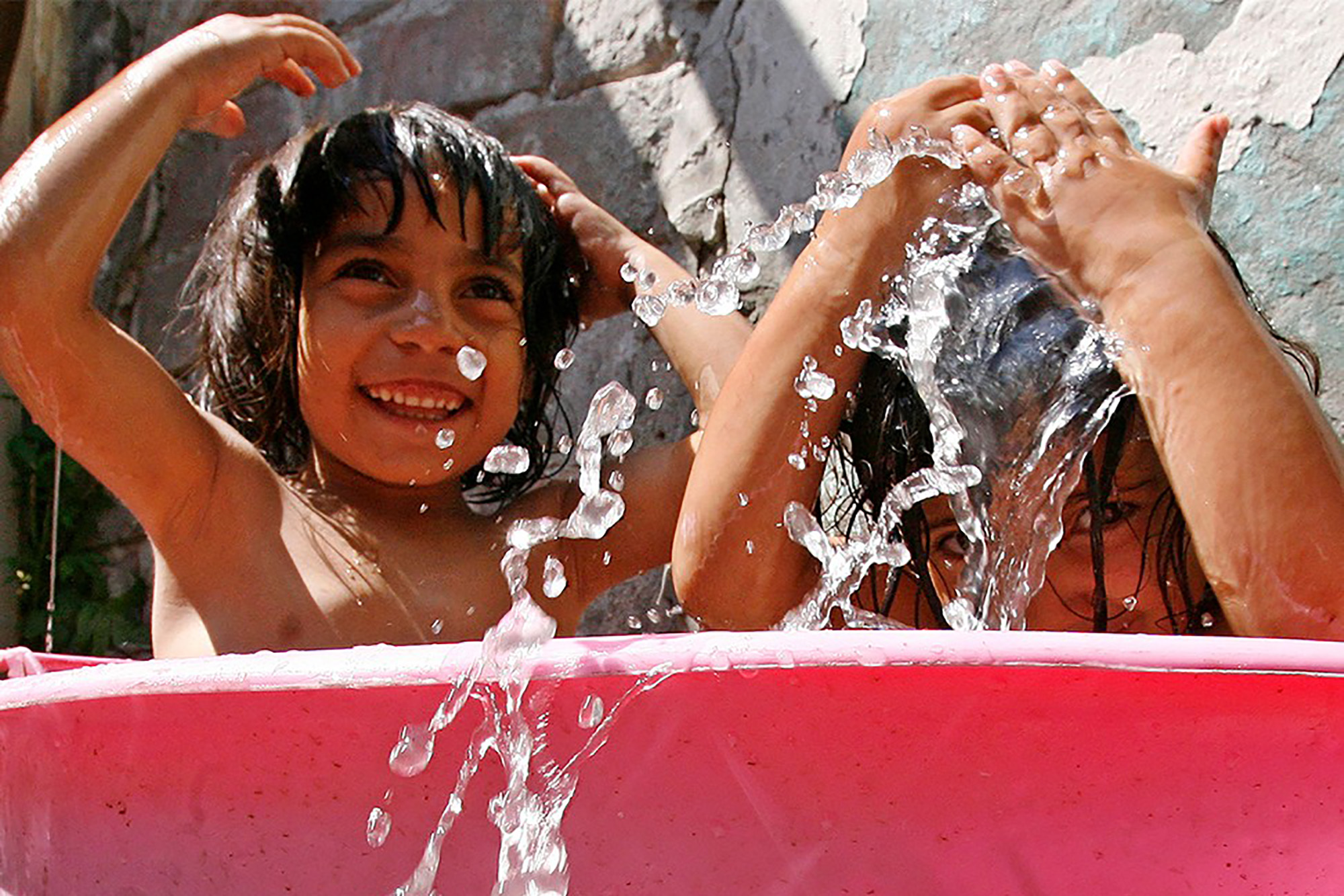 Two Roma children playing with water in a small basin.
