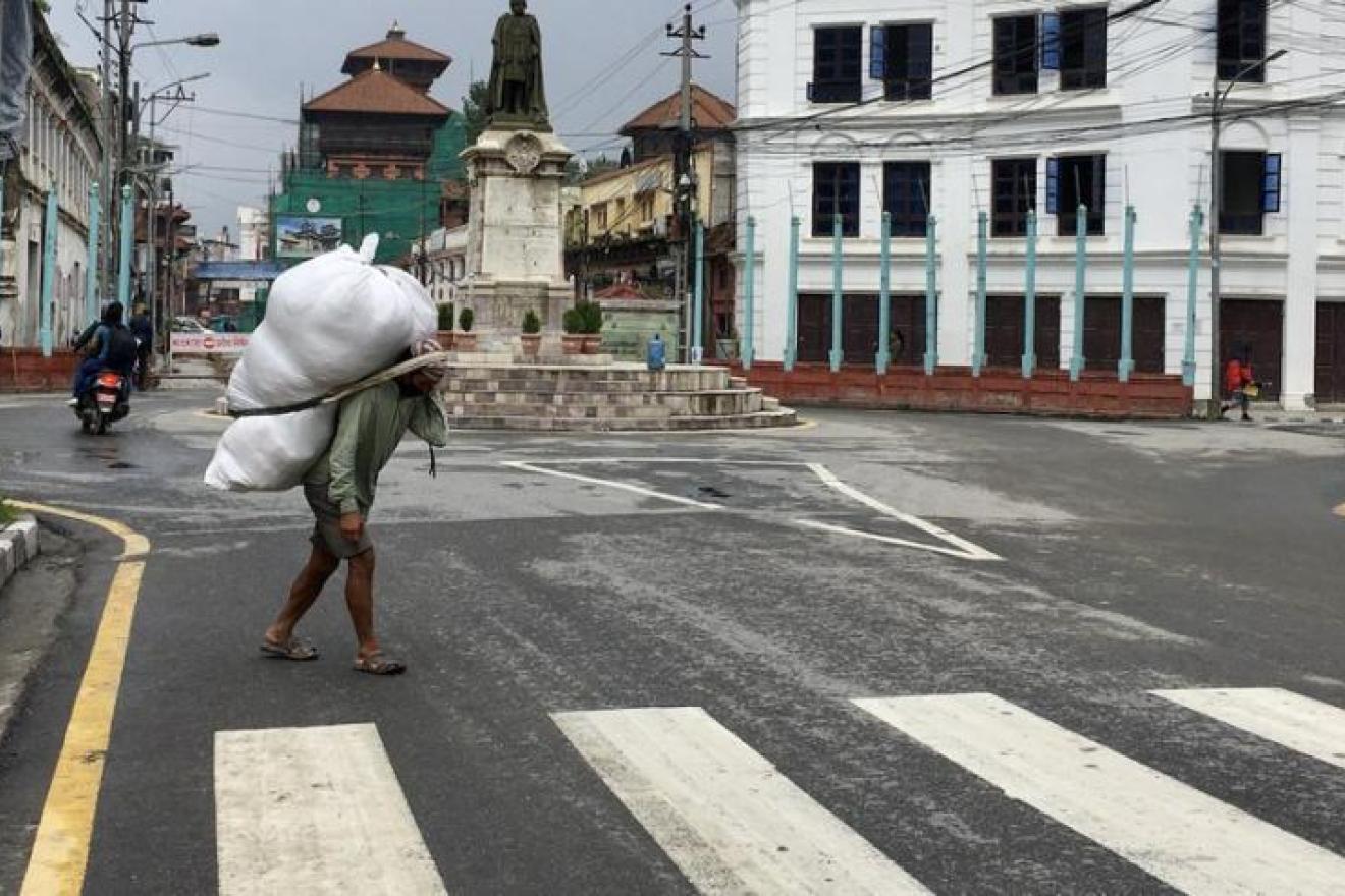 Un hombre cruza una calle vacía transportando una bolsa enorme de mercancía.