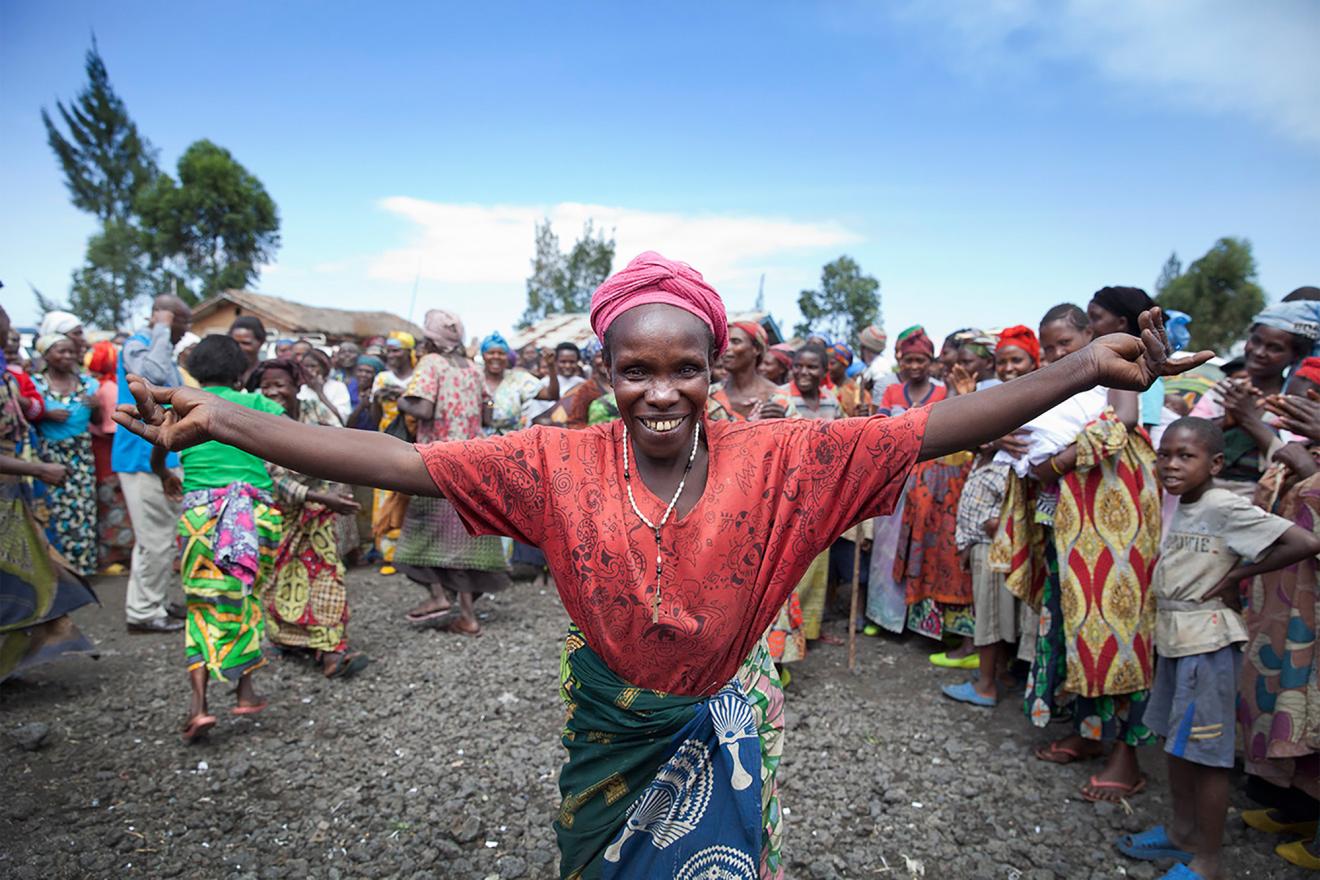 Woman smiling and opening arms with people celebrating in her village.