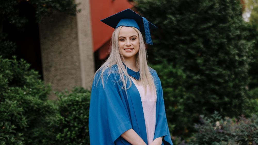 Niamh Carter, in a graduation gown and cap, smiles in front of the Shoalhaven Entertainment Centre. Photo: MIchael Gray