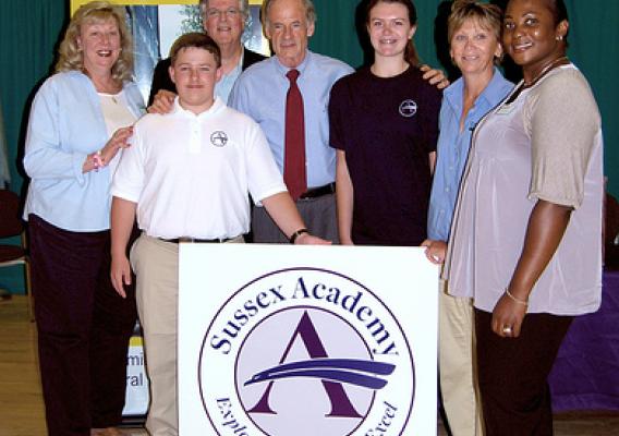 During a tour of the new home of Sussex Academy (l-r) USDA Rural Development Community Program Director Denise MacLeish, USDA Director of Legislative and Public Affairs David Sandretti, rising freshman Cohen Davis, U.S. Senator Tom Carper, rising eight grader Elise Conlin, Acting Delaware/Maryland State Director Kathy Beisner, and Loan Specialist Angela Tilghman stand with Sussex Academy’s new logo. USDA Photo.