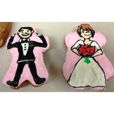 Tray with two people shaped doughnuts and iced to show a groom on the left and a bride on the right.