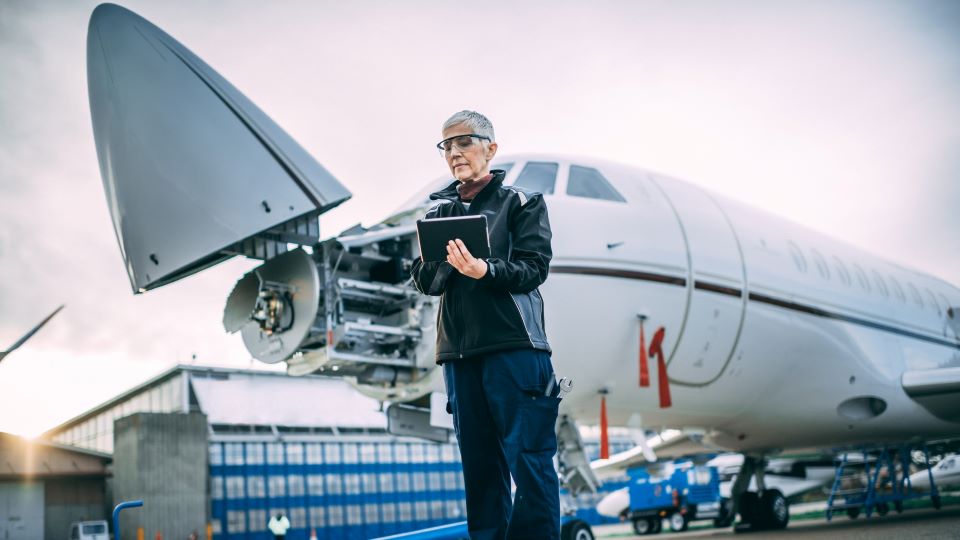 Senior engineer holding digital tablet next to a small private plane with an opened cockpit parked on runway