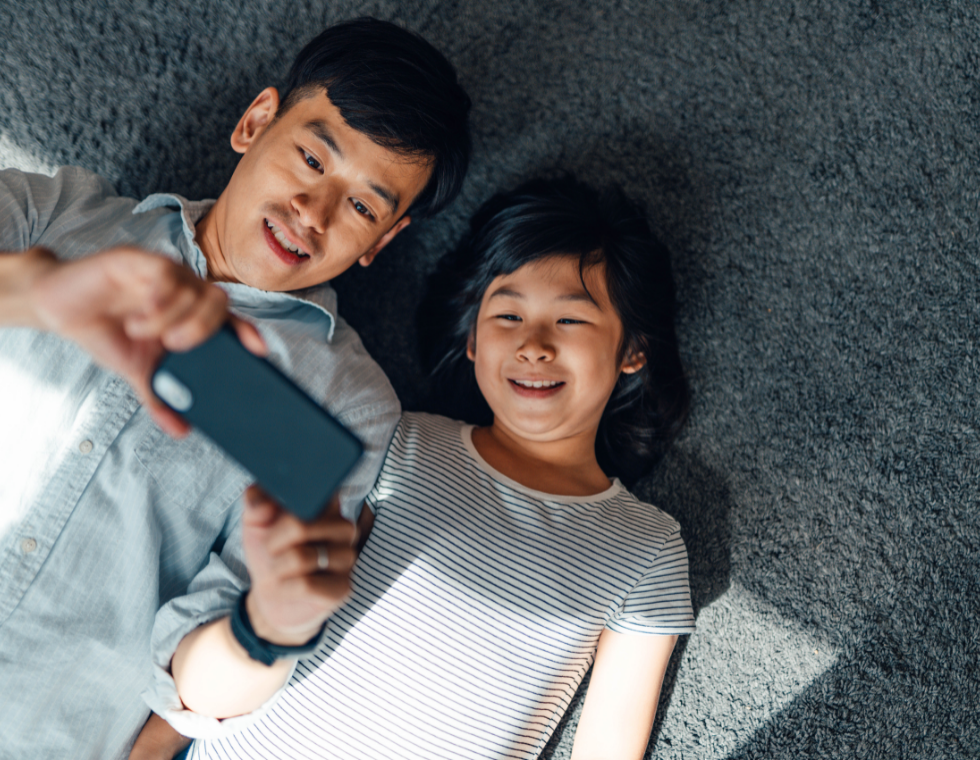 a dad and a child smiling while watching something on the phone