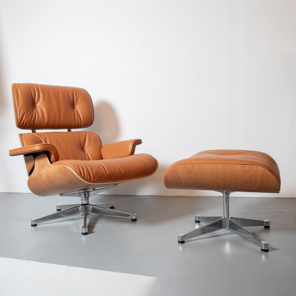 Ein moderner Lounge Chair und Ottoman aus Holzoptik mit brauner Polsterung und silberner Stahlbasis. Der Sessel und Hocker stehen in einem hellen Raum mit schlichtem weißen Hintergrund.