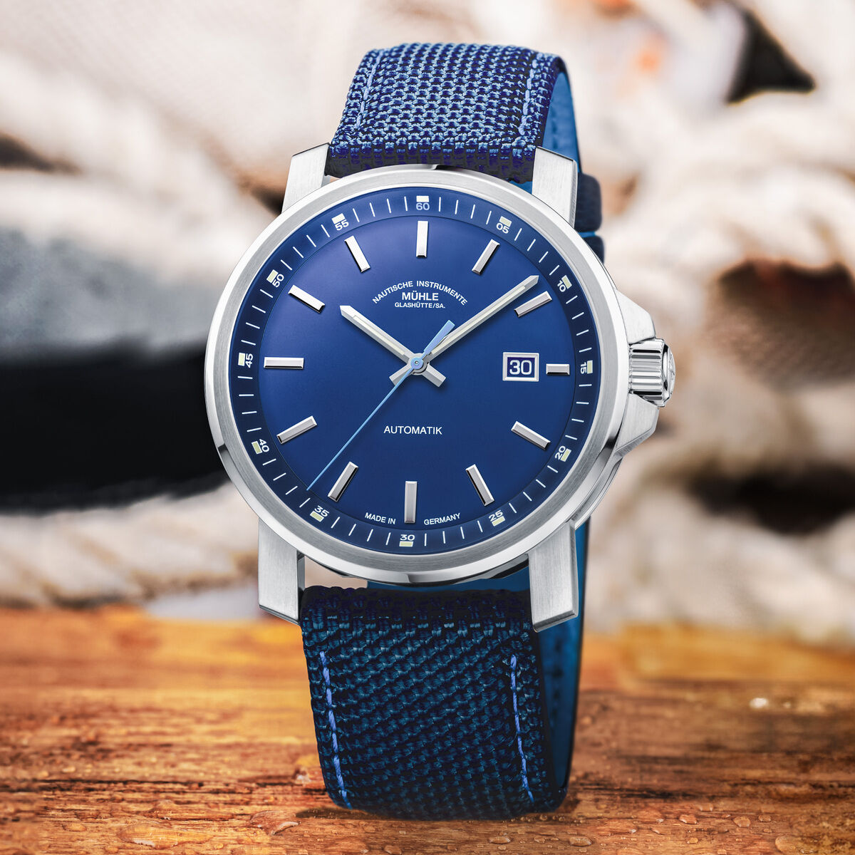 Die ZEIT-Sonderedition »29er Big Deep Blue« von Mühle-Glashütte ist eine hochwertige Herrenarmanduhr mit einem blauen Zifferblatt, Edelstahlgehäuse und blauem Armband, stilvoll platziert auf einer hölzernen Oberfläche mit Wassertropfen im Vordergrund.