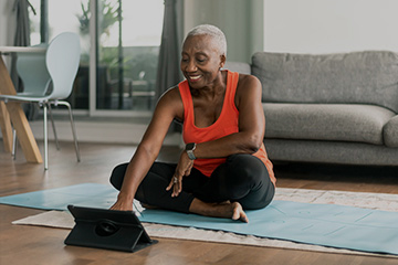 A woman in sportswear sits on the floor of her living room.