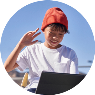 Child smiling while using a laptop in an outdoor setting.