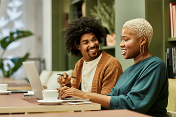 Two people smiling while using a laptop.