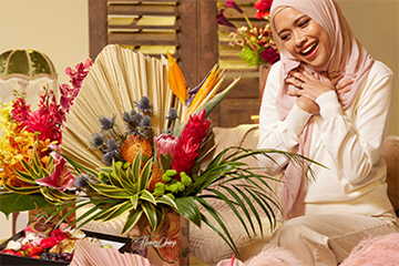 Person sitting in front of a big bouquet of flowers and smiling.