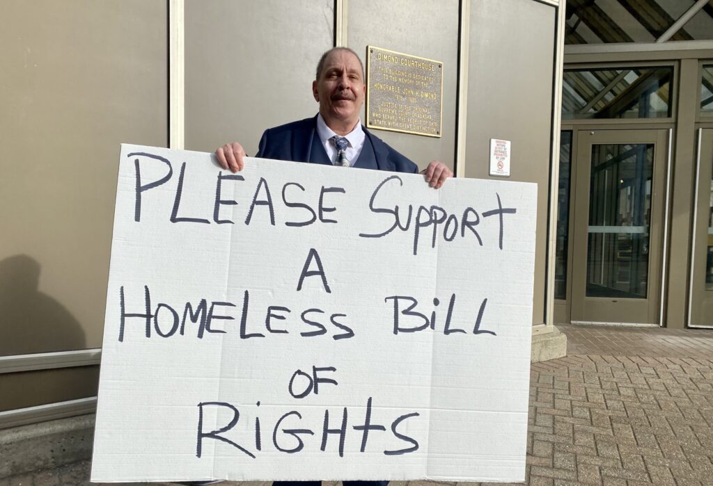 TJ Beers holds a sign to advocate for the rights of people experiencing homelessness outside the state Capitol on April 9, 2024. Beers was homeless for four years and in three states. "I don't know how I survived," he said. (Photo by Claire Stremple/Alaska Beacon)