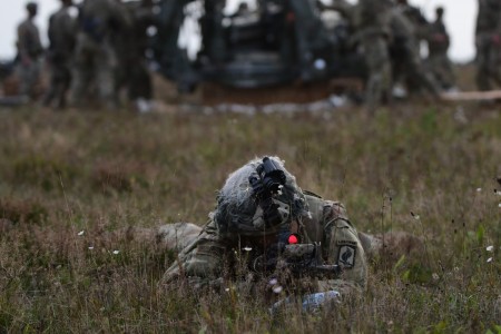A U.S. Paratrooper assigned to Chaos Battery, 4th Battalion, 319th Airborne Field Artillery Regiment, 173rd Airborne Brigade, provides security while others assemble an M777A2 that was delivered during a heavy-drop airborne operation for an artillery live fire at Grafenwoehr, Germany, Oct. 5, 2023.