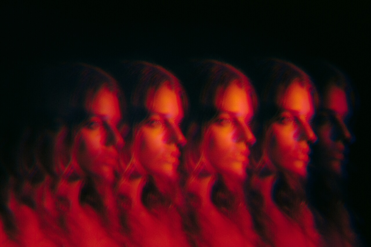 Glitch-style portrait of a woman repeated horizontally. She is lit by a strong red light and the background is dark black.