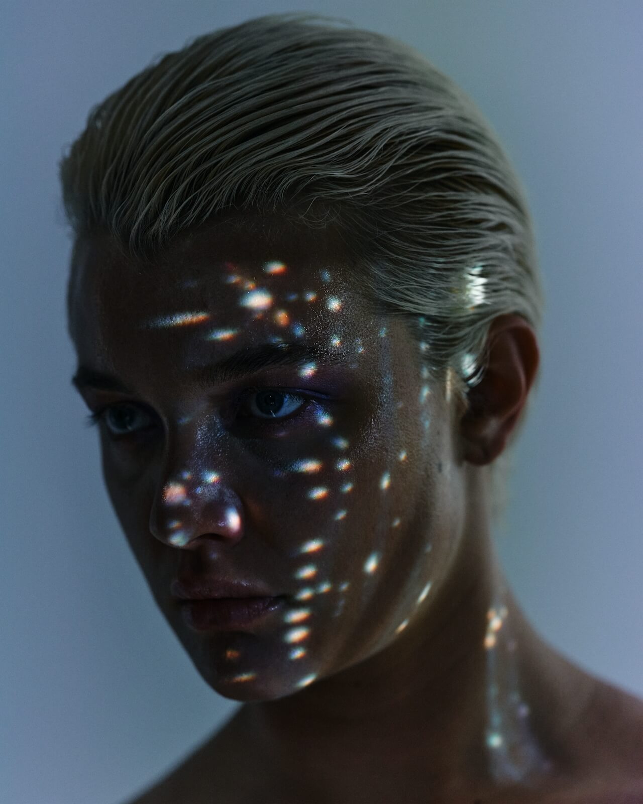 Artistic portrait of a person, their face in darkness apart from speckled lights dancing across their face.