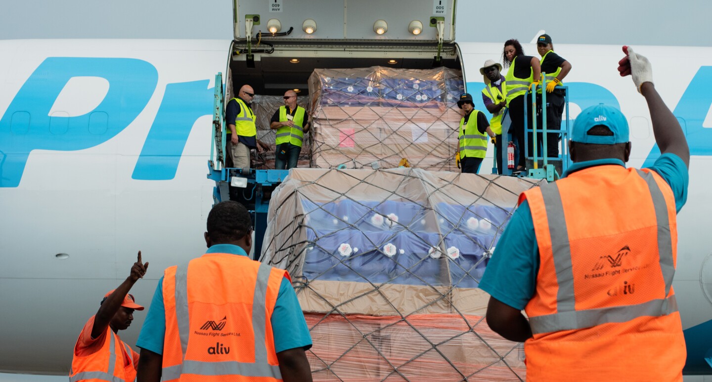 Employees in orange and yellow vests lift cargo supplies onto a Prime Air plane.