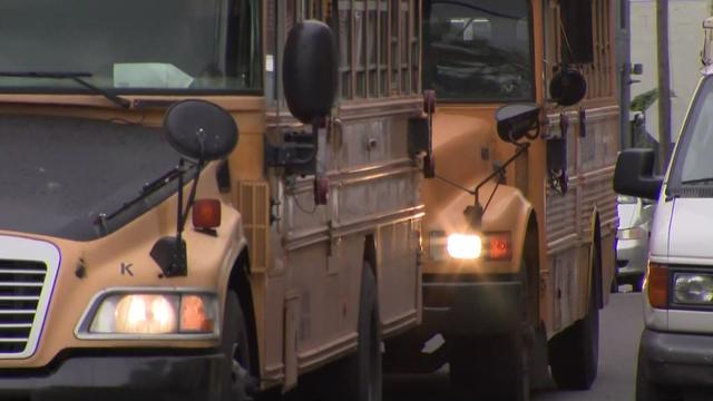 Two yellow school buses behind one another on a street. 