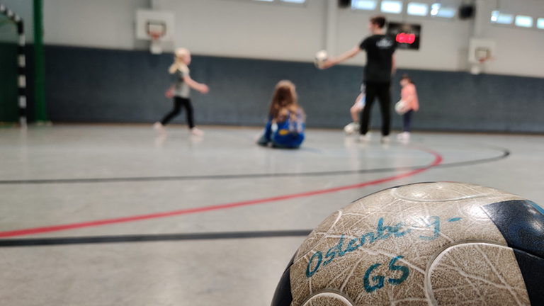 Grundschulkinder beim Fußballspielen in der Halle, im Vordergrund ein Ball