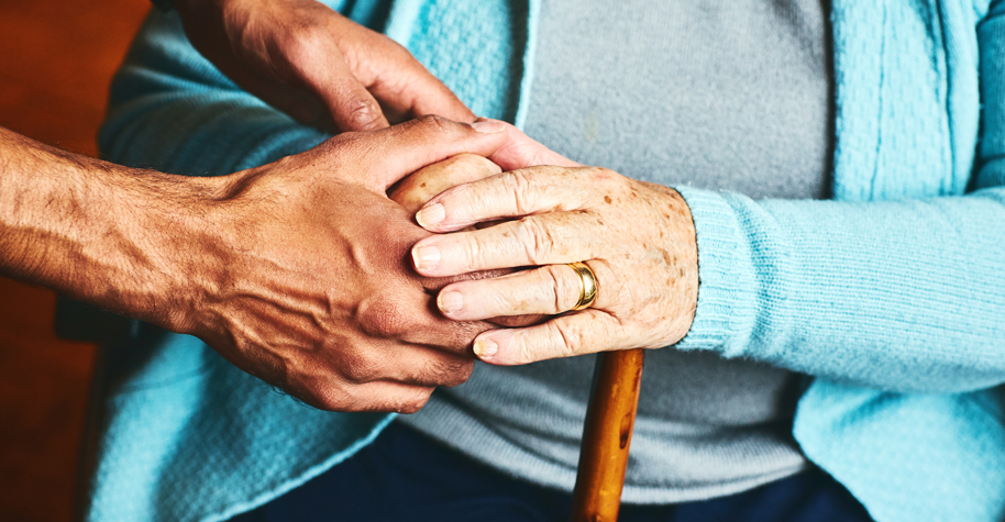 A male caregiver holds the hand of an older woman.
