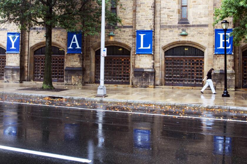 FILE - A woman walks by a Yale sign reflected in the rainwater on the Yale University campus, Aug. 22, 2021, in New Haven, Conn. Columbia University canceled in-person classes Monday, April 22, 2024 and police arrested several dozen protesters at Yale University as tensions on U.S. college campuses continue to grow over the war in the Middle East. (AP Photo/Ted Shaffrey, File)