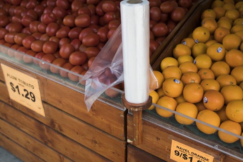 FILE- In this March 27, 2019 file photo, oranges and tomatoes are displayed for sale alongside a roll of plastic bags at a supermarket in New York City's East Village. New York lawmakers are working through the final weekend of March 2019 to pass a budget that would include as one of its proposals a state wide ban on single use plastic bags. (AP Photo/Mary Altaffer, File)