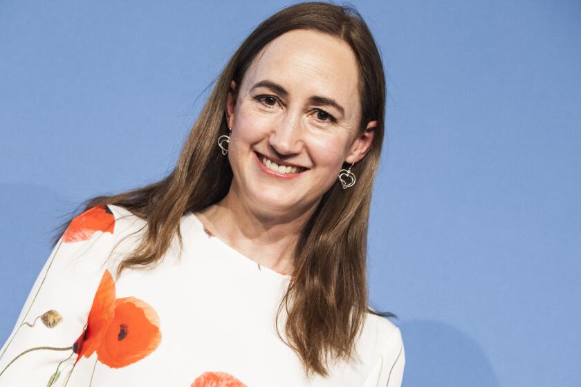 Author Sophie Kinsella smiles while wearing  a white dress with red blooms on it