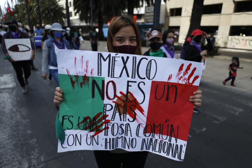 En esta imagen de archivo, una manifestante muestra un cartel con la frase "México no es un país, es una fosa común con un himno nacional" durante una marcha por el Día Internacional de la Mujer, en Ciudad de México, el 8 de marzo de 2021. Mujeres de todo el mundo exigirán igualdad salarial, derechos reproductivos, educación, justicia y otras necesidades esenciales durante las manifestaciones para conmemorar el Día Internacional de la Mujer el 8 de marzo.