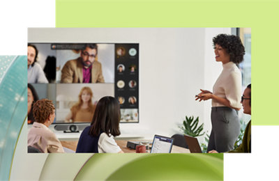 A woman presents to colleagues in a conference room with a large screen showing remote participants in a video call.