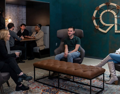 A group of people in a modern office lounge, some seated and others standing, engaged in conversation.