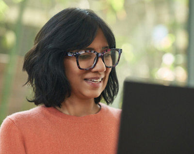 A woman with spectacles smiling and working on her laptop