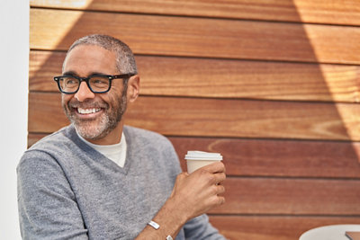 A person wearing glasses, holding a cup and smiling.