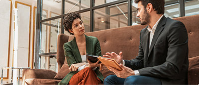 Two persons sitting, holding tablets and discussing on some topic.