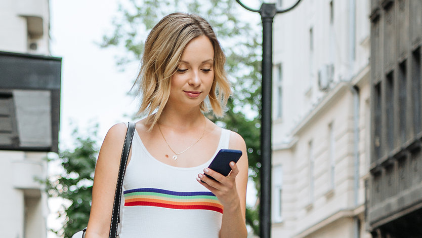 A young woman checks her phone on a busy city sidewalk.