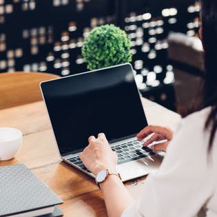 A woman sits at a desk and types on a mac. 