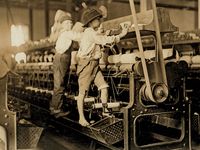 Young boys working in a thread spinning mill in Macon, Georgia, 1909. Boys are so small they have to climb onto the spinning frame to reach and fix broken threads and put back empty bobbins. Child labor. Industrial revolution