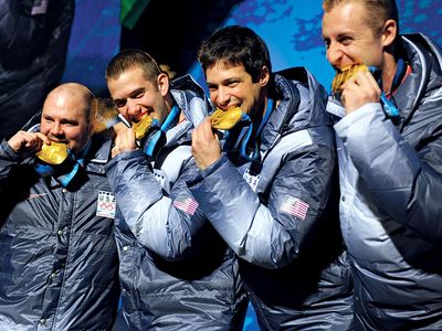 Former U.S. Army World Class Athlete Program bobsledder Steven Holcomb, left, and teammates Justin Olsen, Steve Mesler and Curt Tomasevicz bite their gold medals Saturday night at Whistler Medals Plaza after winning the Olympic four-man bobsled, 2010.