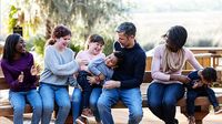 A blended family having fun at the park sitting on a bench together.