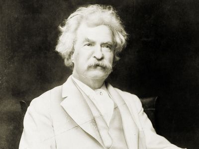 Samuel Clemens aka Mark Twain, three-quarter length portrait, seated, facing slightly right, with cigar in hand.