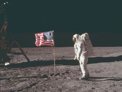 (Buzz Aldrin) stands next to the U.S. flag at Tranquility Base on the Moon during NASA's Apollo 11 mission, July 20, 1969. Aldrin's forward-leaning stance was the normal resting position of an astronaut wearing the life-support pack.