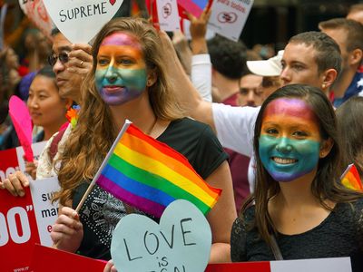Young women with rainbow painted faces - symbol of lesbian, gay, bisexual and transgender - LGBT - watch the San Francisco Pride Parade in 2015. Gay pride human rights civil rights spectators California