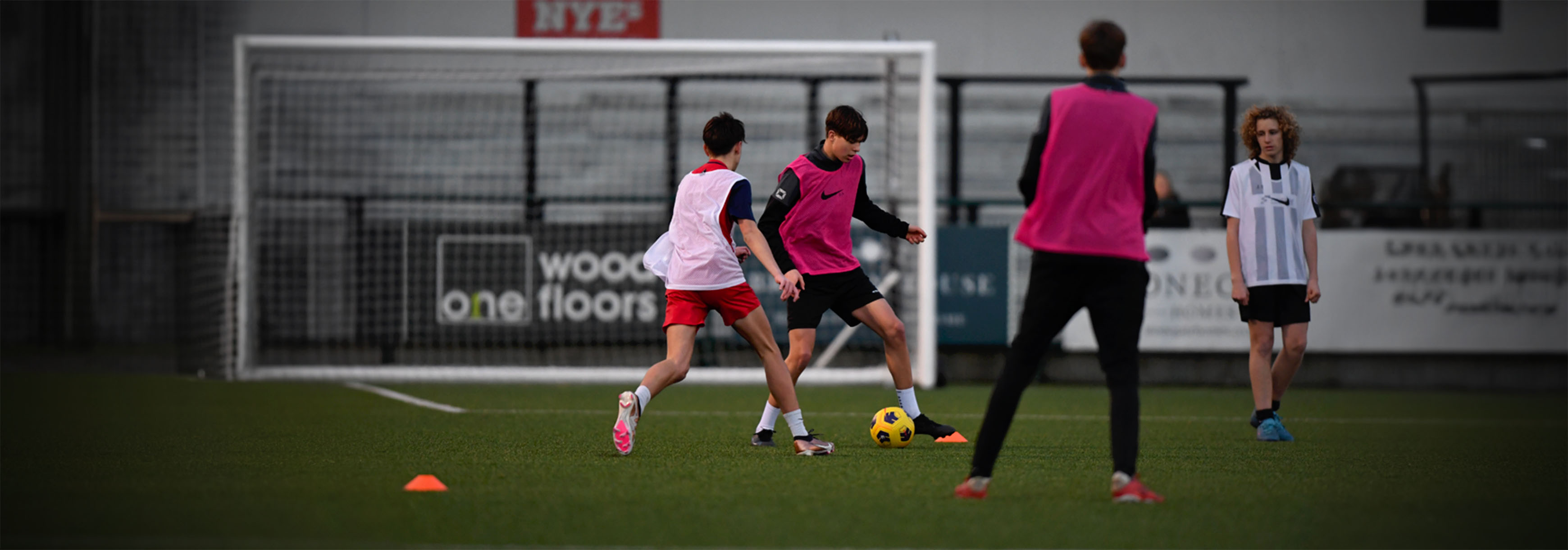 A group of teenagers wearing pink and white bibs are playing against each other. A player in a pink bib receives the ball while under pressure from an opponent.