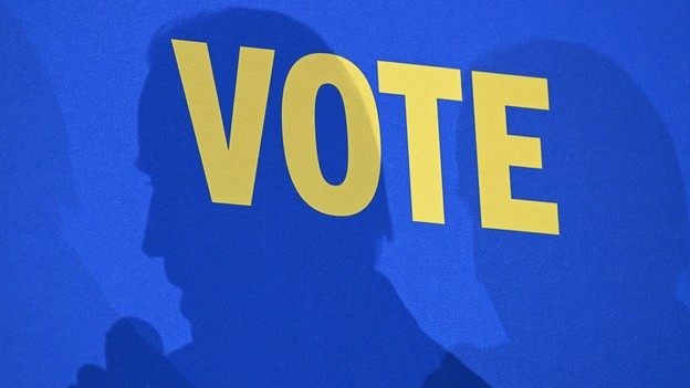 A photo of the word "vote" on a wall, with Joe Biden's shadow cast over it