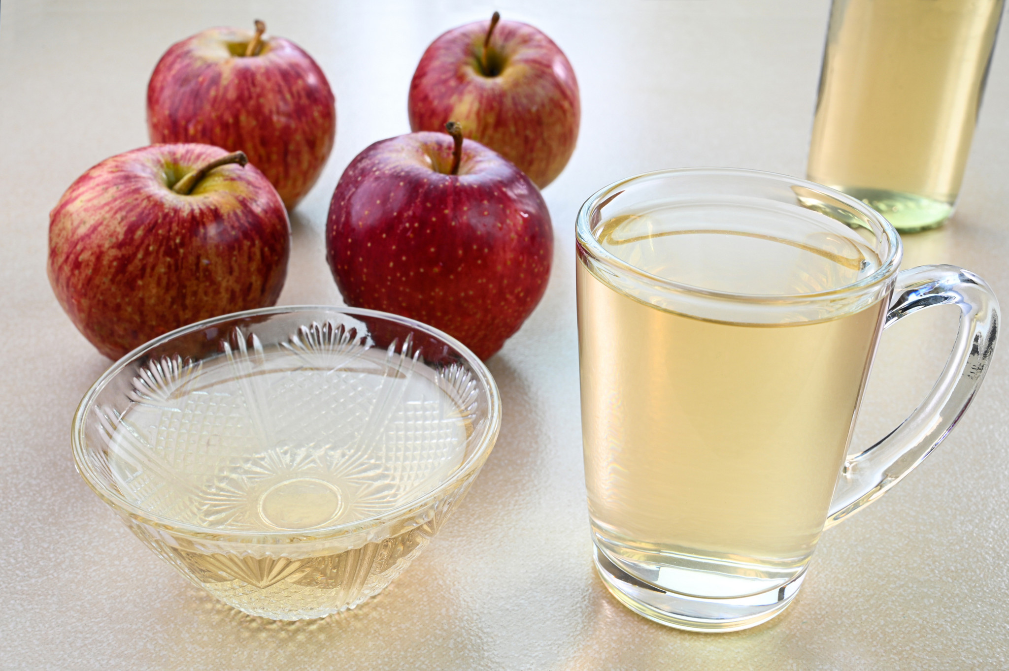 Apple cider vinegar in a glass cup and apples in the background.
