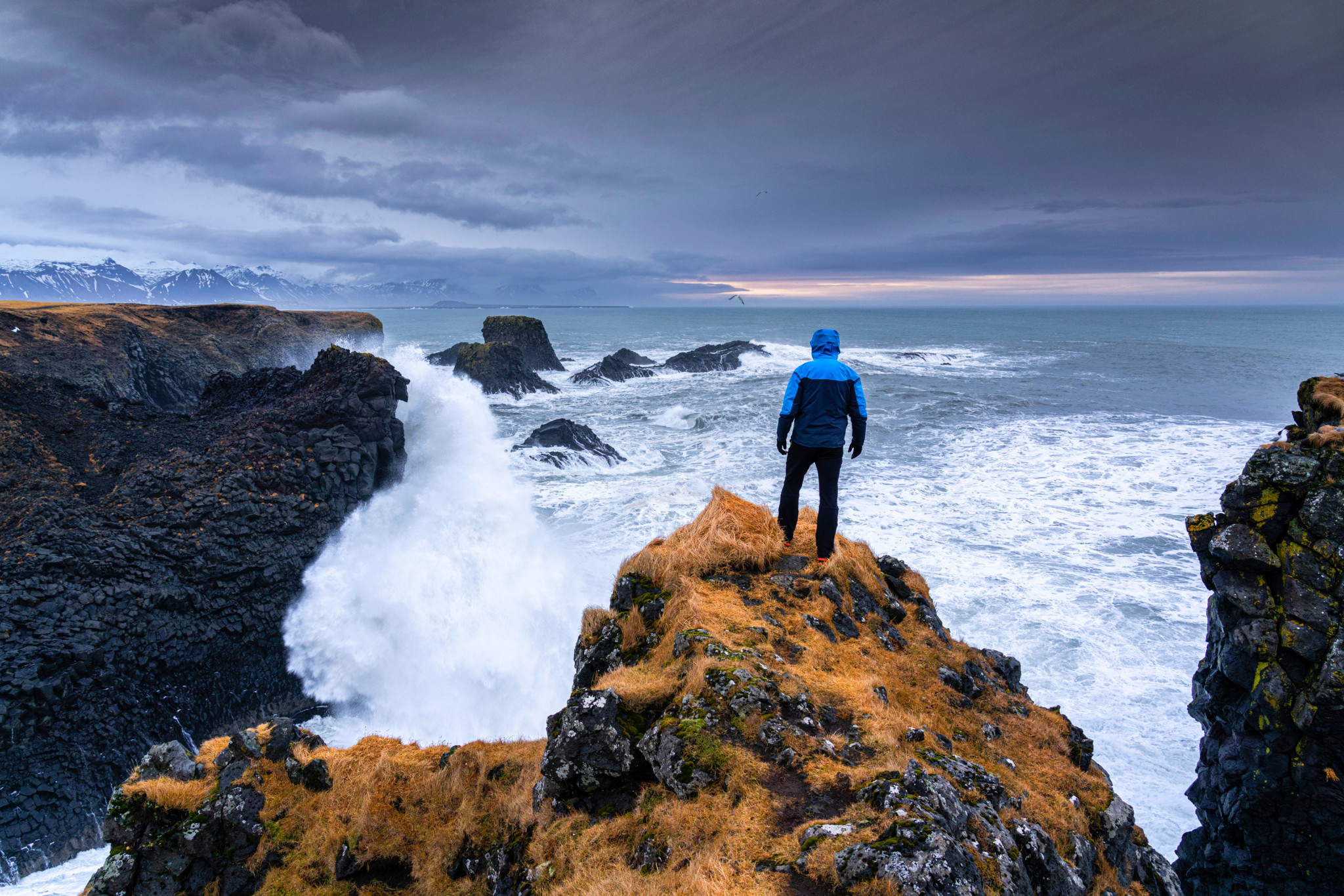 Iceland, Vesturland region, Snaefellsnes peninsula: rear view of a man gazing at the basaltic coastline with rough sea on a winter day.