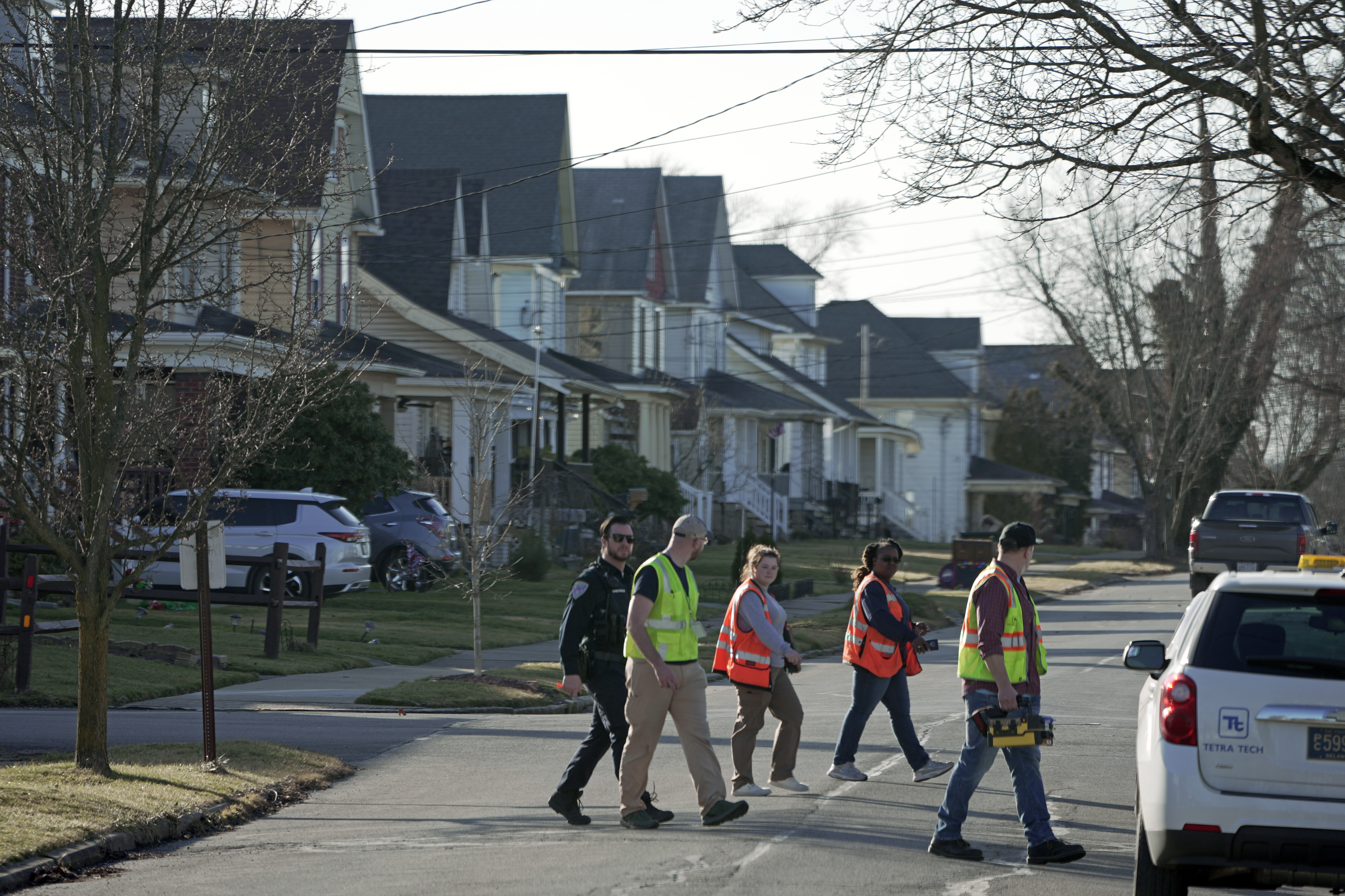 People in neon safety vests walk across a suburban street.