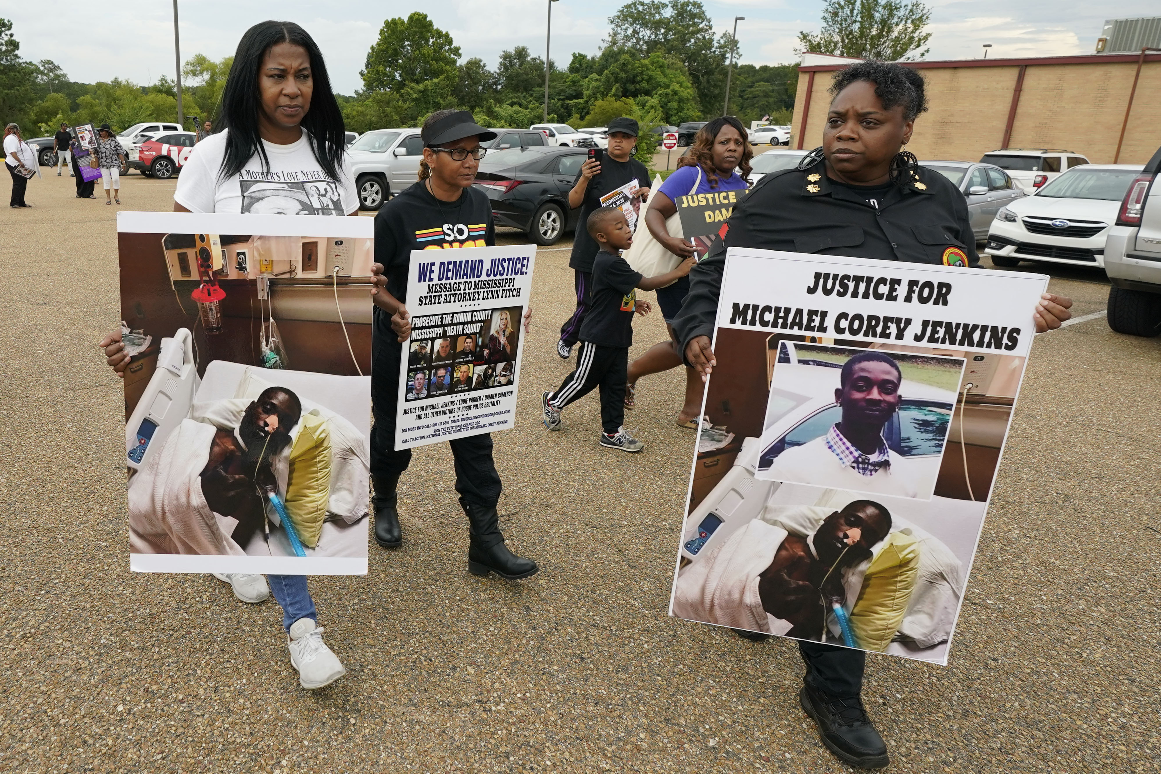 Black women hold signs displaying Parker and Jenkins’ wounds that read “We Demand Justice” and “Justice for Michael Corey Jenkins.”