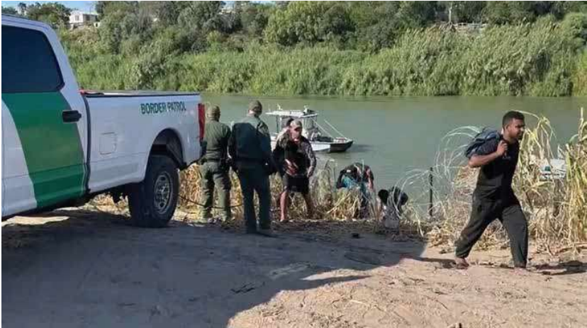 People stand beside a pickup truck at the edge of a river.