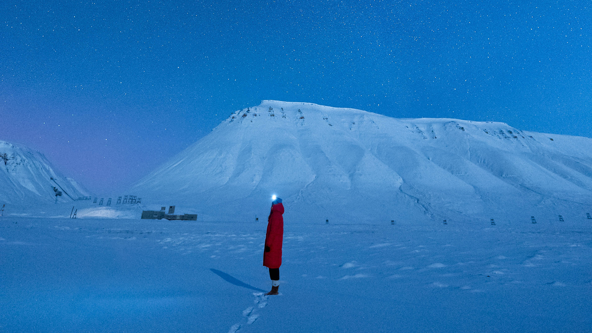A woman in a red coat stands in a dark blue snowy landscape.