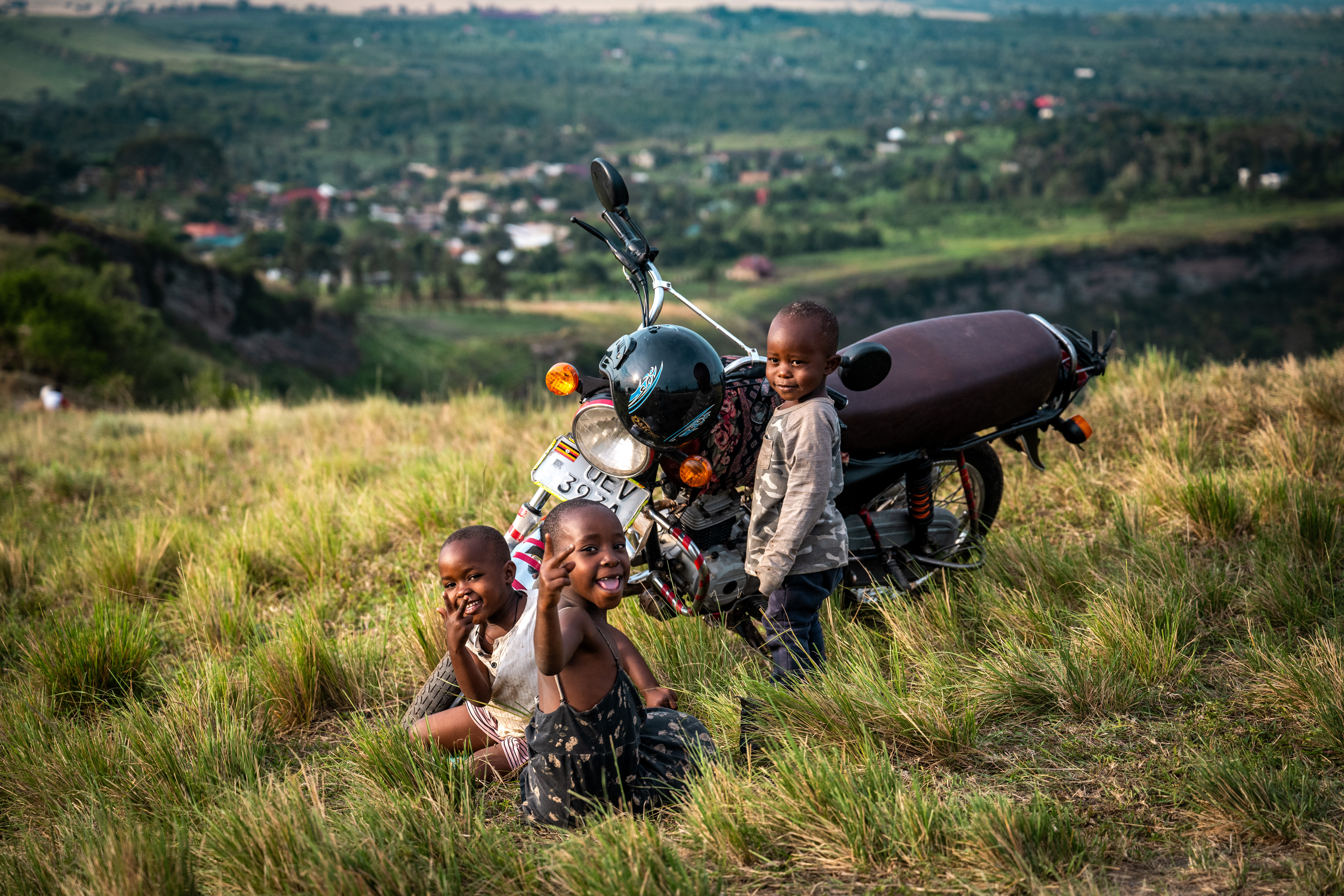 Three Black children on a green hilltop with a motorbike.