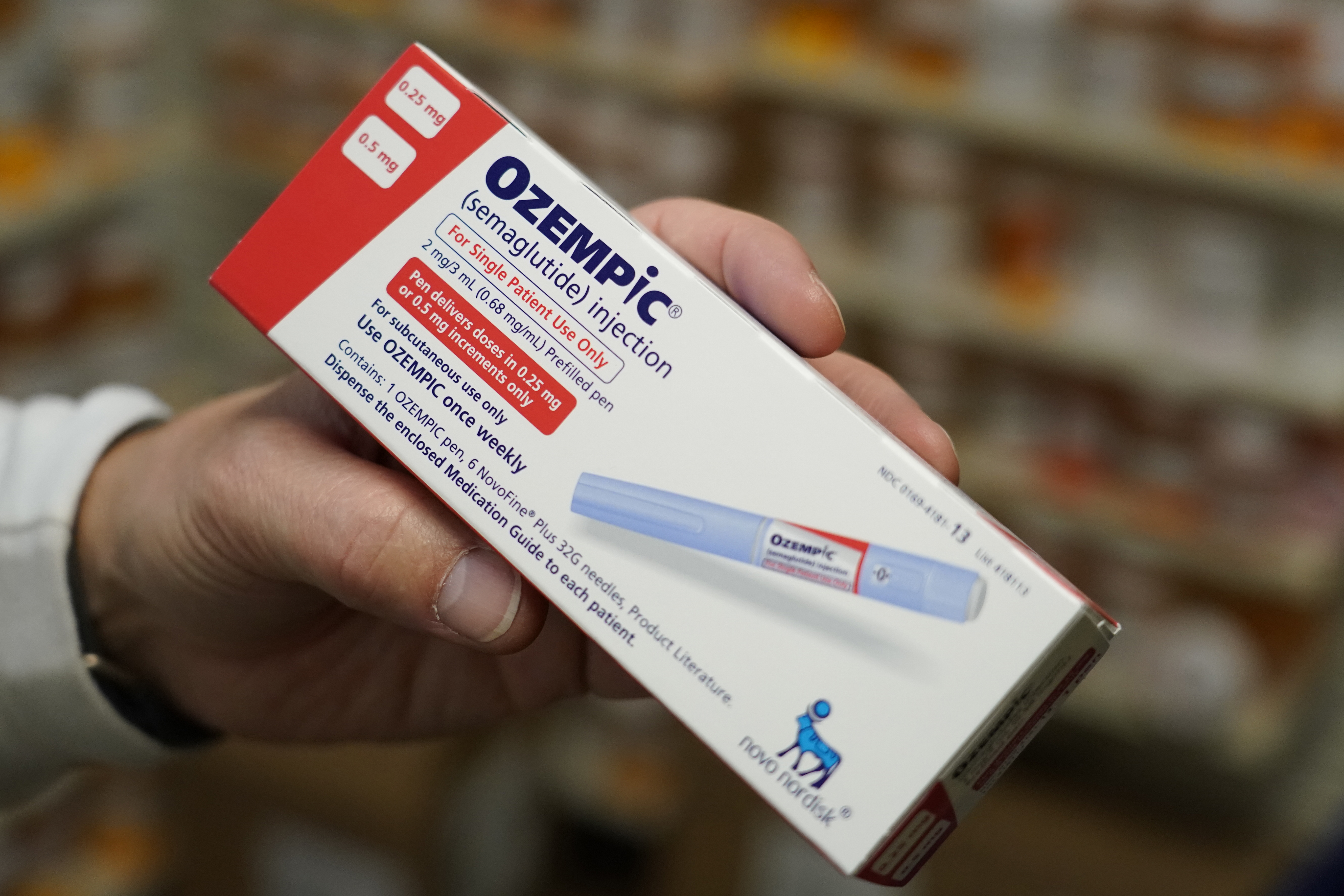 A pharmacist holds a box of Ozempic with the label visible.